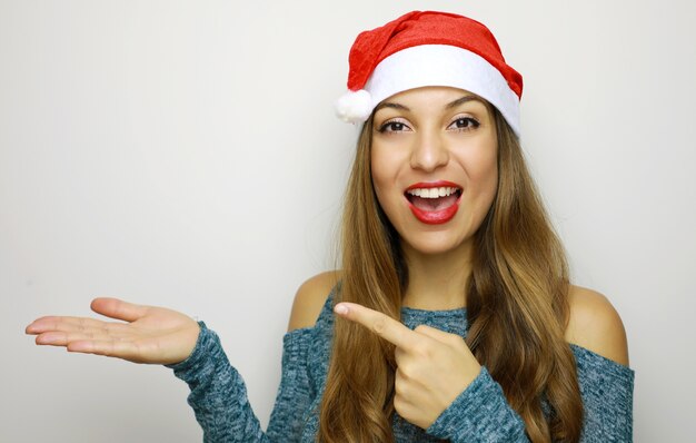 Mujer con sombrero de Navidad sonriendo mientras presenta con la mano y apuntando con el dedo