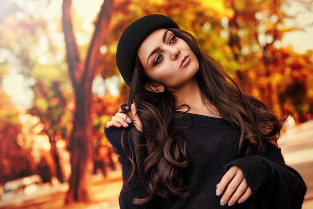 Mujer con sombrero negro en el fondo de las hojas de otoño