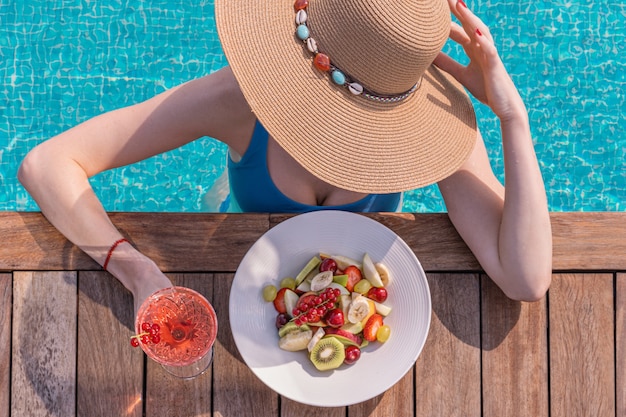 Foto mujer con sombrero de paja y bikini con bayas junto a la piscina