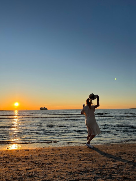 mujer con sombrero de paja caminando por la playa al atardecer