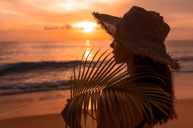 Mujer con sombrero de paja en la playa al atardecer