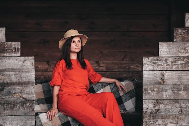 Mujer con sombrero de paja vestida con ropa roja sentada en el fondo de una casa de madera