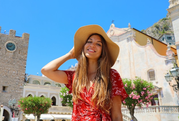 Mujer con sombrero de paja y vestido rojo con la aldea de Taormina, Sicilia, Italia