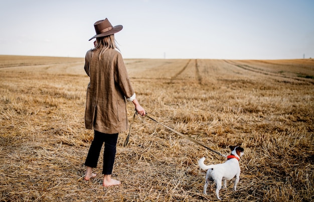 Mujer con sombrero con perro en campo de trigo