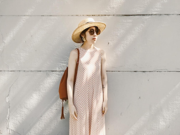 Mujer con sombrero de pie contra la pared blanca