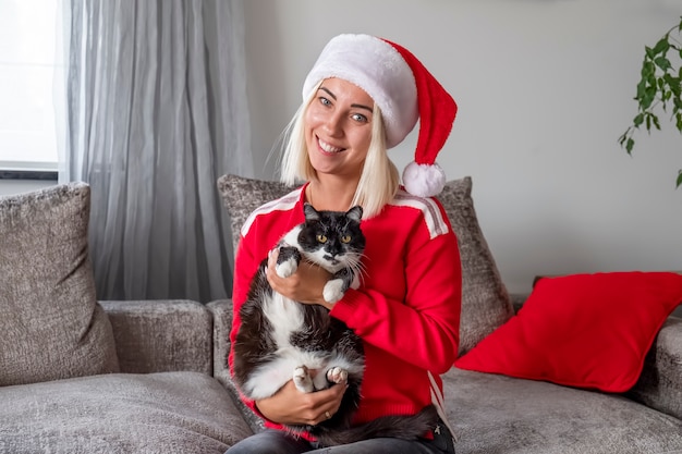 Mujer con sombrero rojo de Navidad sentado en el sofá con gato.