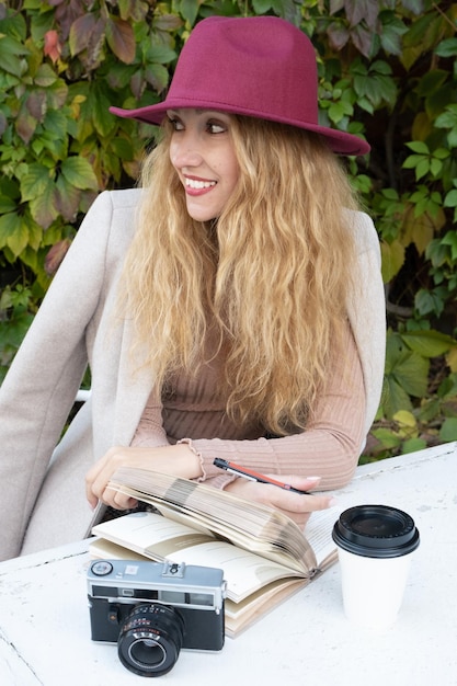 Una mujer con un sombrero rojo sonríe sentada en una mesa en un café callejero en otoño