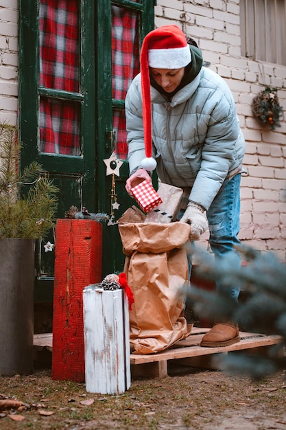 Mujer con sombrero de Santa lleva una bolsa de regalos desde la puerta principal del porche de la casa