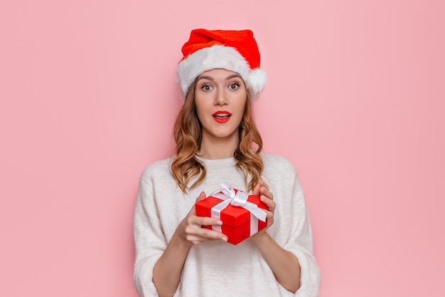 Mujer con sombrero de santa sonriendo y sosteniendo una caja de regalo roja