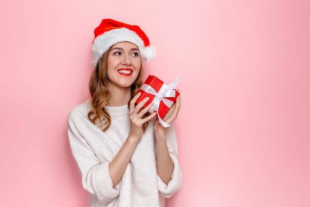 Mujer con sombrero de santa sonriendo y sosteniendo una caja de regalo roja