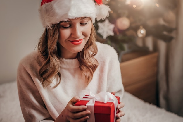 Mujer con sombrero de santa sonriendo y sosteniendo una caja de regalo roja