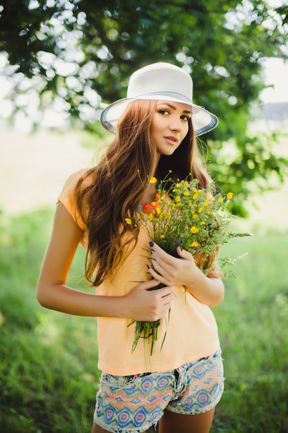 Mujer con un sombrero sujetando flores