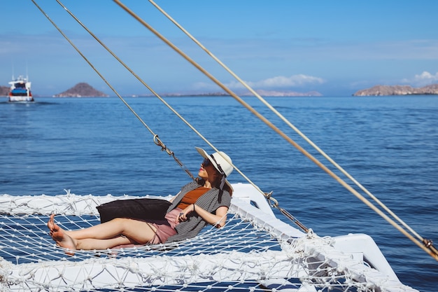 Mujer con sombrero de verano y gafas de sol relajándose en catamarán net disfrutando de vistas al mar