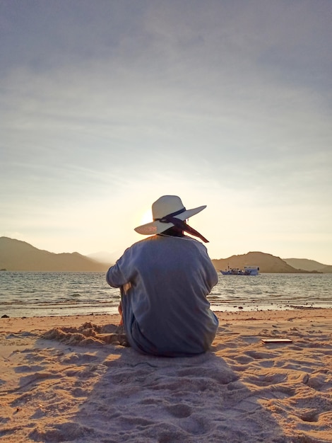 Foto mujer con sombrero de verano sentado en la playa contra la luz del sol