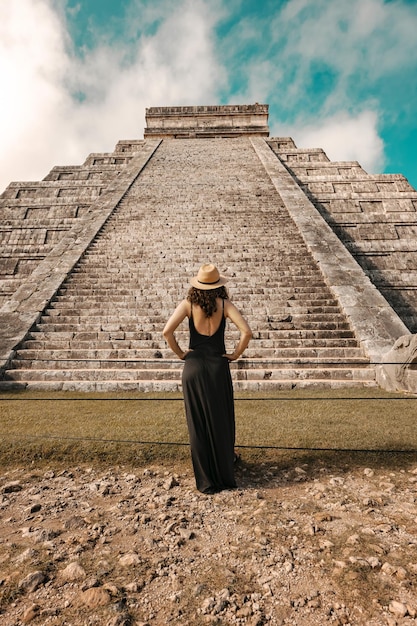 Mujer con sombrero y vestido negro (vista posterior, no reconocida) frente a la pirámide de Chichen-Itza en