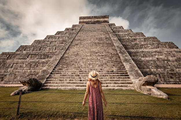 Mujer con sombrero y vestido rojo frente a la pirámide de Chichen-Itza en Yucatán, México