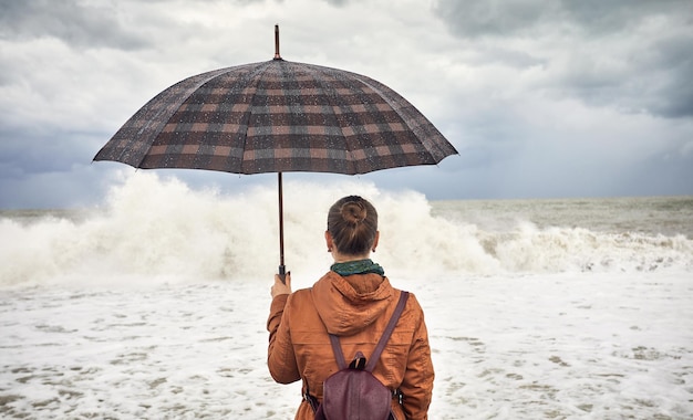 Mujer con sombrilla cerca del mar tormentoso