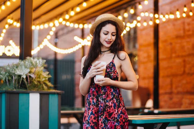 Mujer soñadora con cabello oscuro con sombrero y vestido con estampado de flores