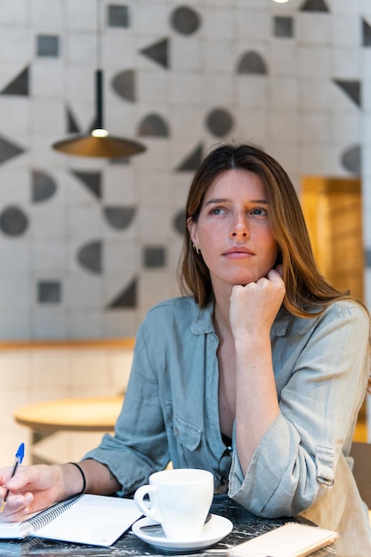 Mujer soñadora con cuaderno y té en el café