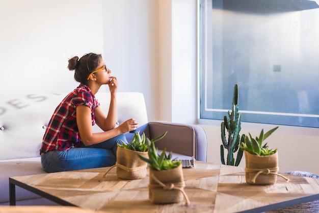 Foto mujer soñadora mirando por la ventana en casa mientras usa una computadora portátil y bebe café