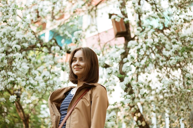 Foto mujer soñadora relajándose en un jardín floreciente en primavera y parada cerca de un árbol