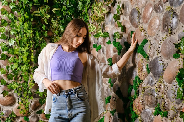 Mujer soñadora tocando el muro de piedra cubierto de plantas