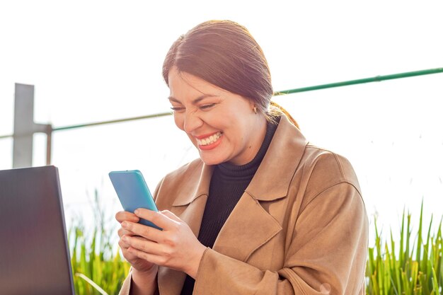 La mujer sonríe emocionada sosteniendo el teléfono en su cara posiblemente recibiendo buenas noticias o ganando un premio