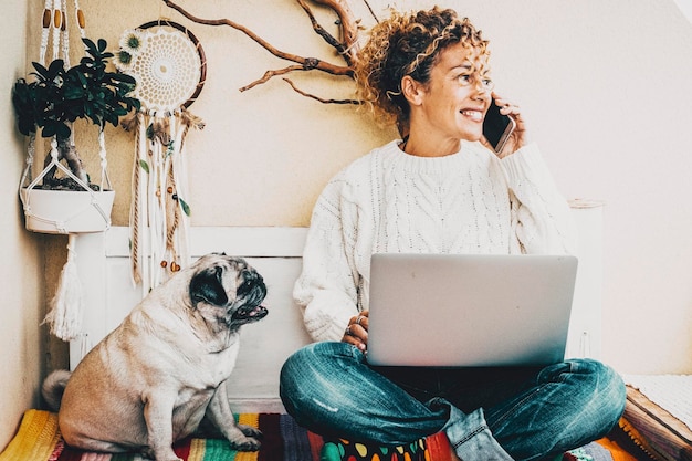 La mujer sonríe y habla por teléfono con su mejor amigo, el perro, siéntese cerca de ella. La gente moderna, un estilo de vida de trabajo inteligente, usa la computadora y disfruta de la amistad animal con un pug Concepto de pareja