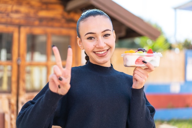 Una mujer sonríe y sostiene un yogur con la palabra desayuno al fondo.