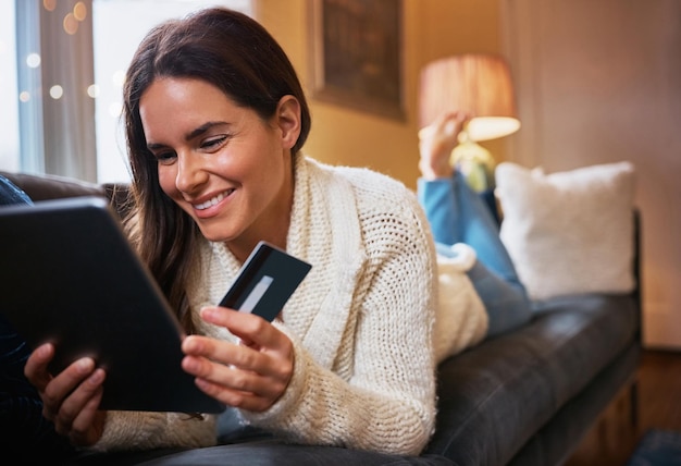 La mujer sonríe y tableta con tarjeta de crédito en el sofá para compras en línea pago y plan de ahorro persona femenina en casa y feliz en la sala de estar en el sofa para banca por Internet inversión y descuento