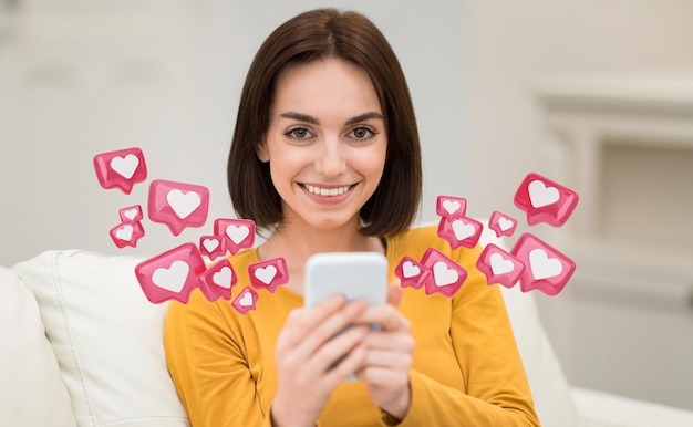 Mujer sonriendo al teléfono inteligente rodeada de corazones sentada en el sofá