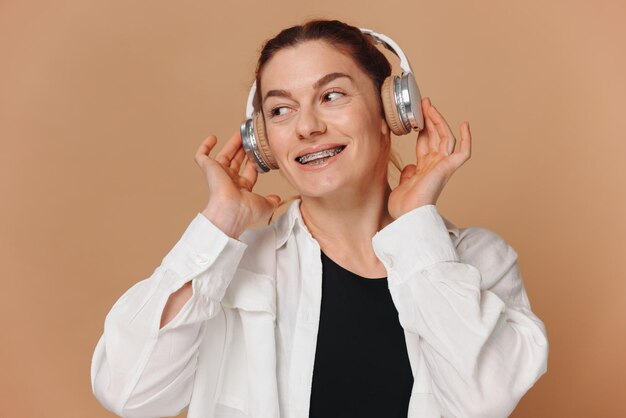 Foto mujer sonriendo con aparatos ortopédicos en los dientes y escuchando música en auriculares sobre un fondo beige