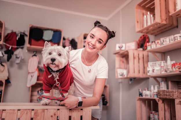 Foto mujer sonriendo. atractiva mujer joven de pelo oscuro sonriendo después de poner ropa roja en el perro