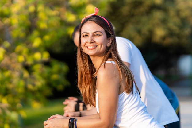 Mujer sonriendo a la cámara mientras descansa en una barandilla al aire libre con sus amigos