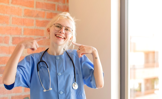 Mujer sonriendo con confianza apuntando a su propia sonrisa amplia, actitud positiva, relajada y satisfecha