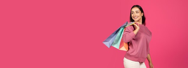 Mujer sonriendo mientras lleva bolsas de compras coloridas contra un fondo rosa