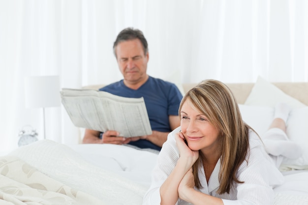 Mujer sonriendo mientras su marido está leyendo