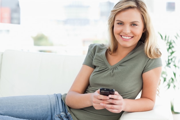 Mujer sonriendo y mirando delante de ella mientras usa su teléfono