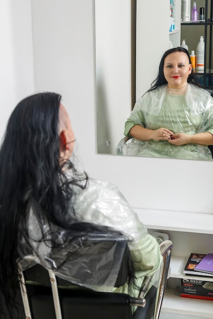 Foto mujer sonriendo con la mitad de la cabeza rapada en una silla de peluquero reflejada en el espejo foto vertical