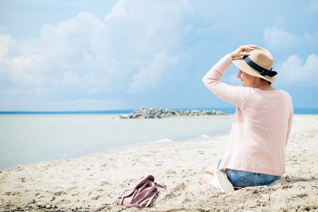 Mujer sonriendo y sentada en la playa contra el mar