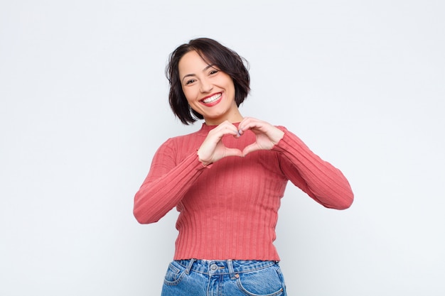 Mujer sonriendo y sintiéndose feliz, linda, romántica y enamorada, haciendo forma de corazón con ambas manos