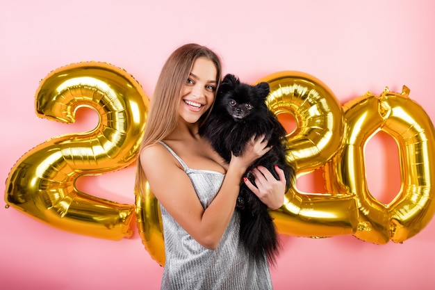 Mujer sonriendo con spitz japonés perro negro y globos de oro 2020 año nuevo aislados en rosa