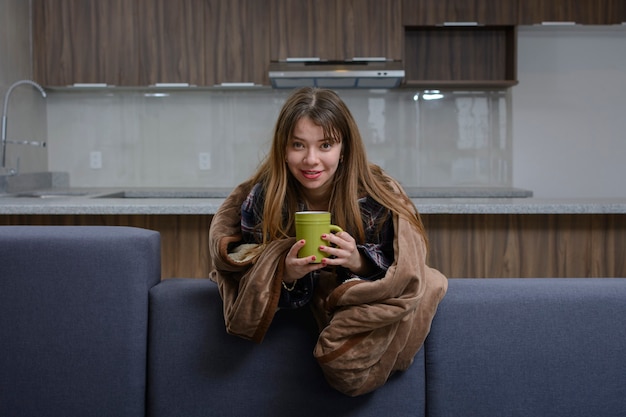 Mujer sonriendo con una taza de café en la mano cubierta con una manta en un día frío