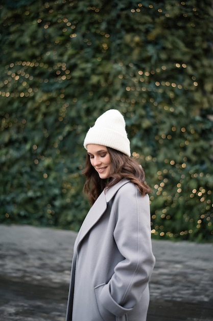 Foto mujer sonriente con abrigo gris y sombrero blanco en el fondo del árbol de navidad concepto de invierno