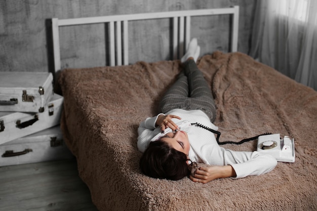 Mujer sonriente acostada en la cama y hablando por teléfono en casa