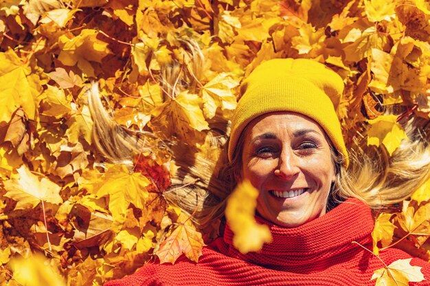 Mujer sonriente acostada sobre hojas amarillas y rojas en la vista del parque desde arriba