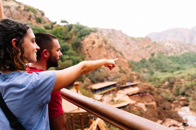 Mujer sonriente al lado de un hombre que señala al horizonte delante de un paisaje árido con pequeñas casas. Cascadas de Ouzoud en Marruecos