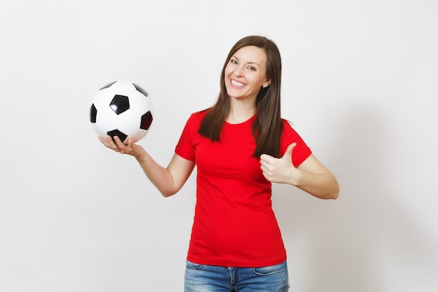 Mujer sonriente alegre joven europea, fanático del fútbol o jugador en uniforme rojo que sostiene el balón de fútbol, mostrando el pulgar hacia arriba aislado sobre fondo blanco. Deporte, jugar al fútbol, animar, concepto de estilo de vida saludable.