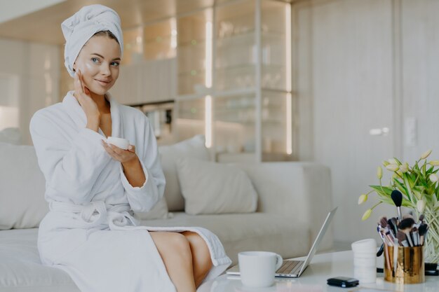 Mujer sonriente aplica crema nutritiva en la cara