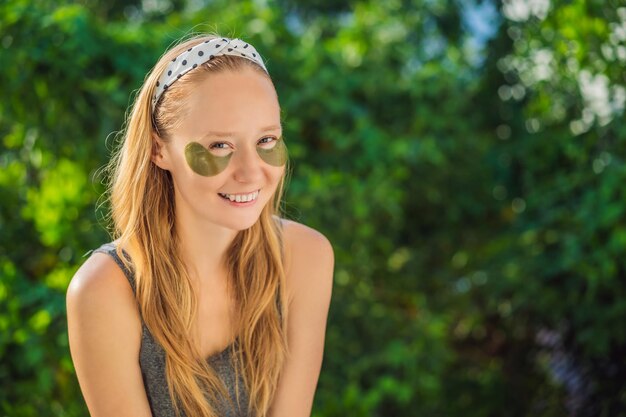 Mujer sonriente aplicando parches de hidrogel para el cuidado de los ojos hidratando la piel debajo de los ojos disfrutando de los procedimientos de cuidado de la piel